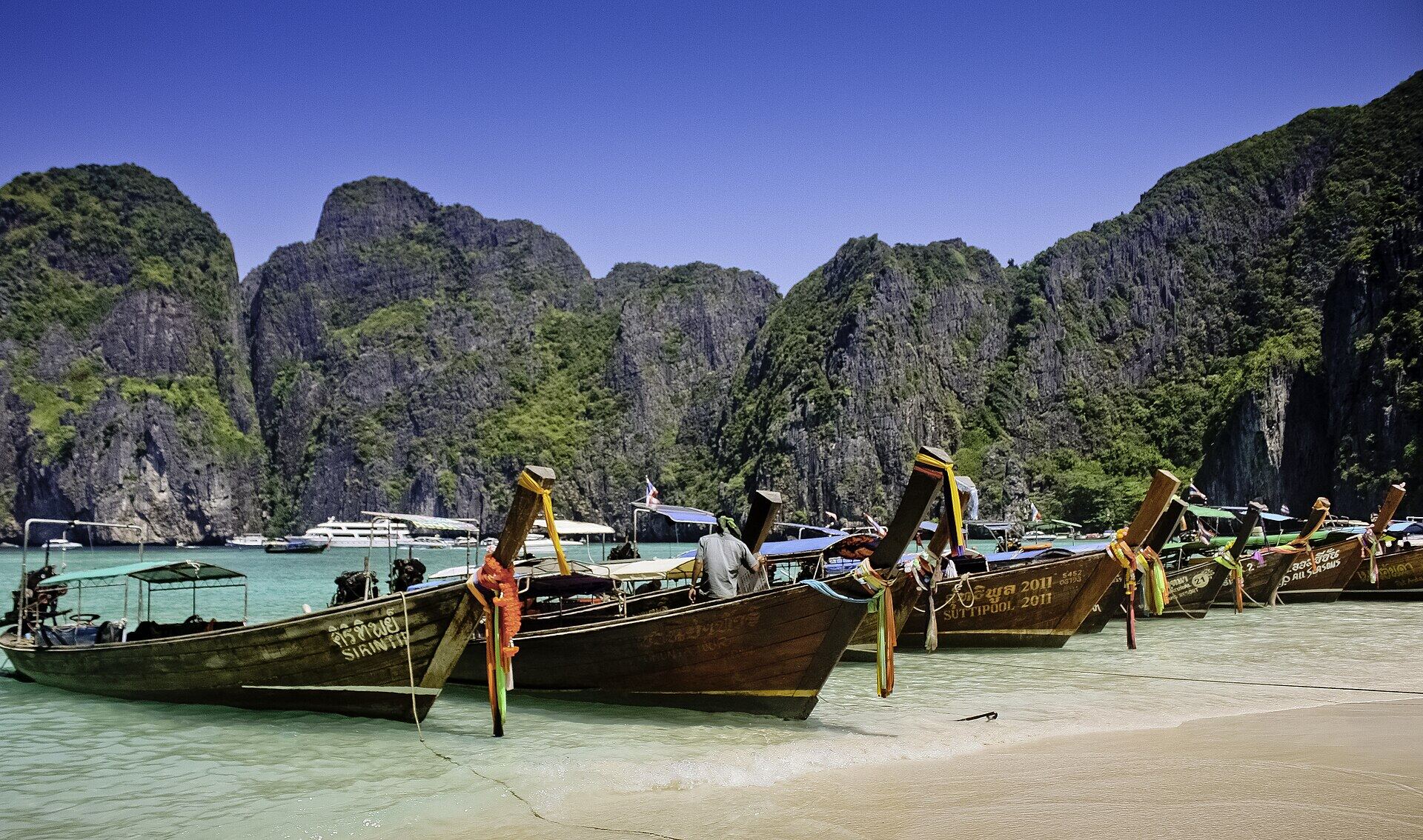 A longtail boat anchored beneath limestone cliffs at Maya Bay, Krabi
